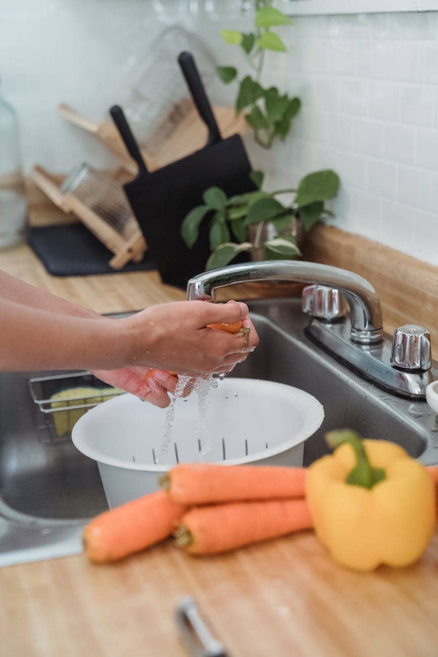 a person washing vegetables on the sink